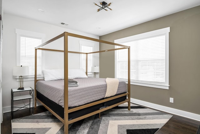 bedroom featuring visible vents, multiple windows, baseboards, and wood finished floors