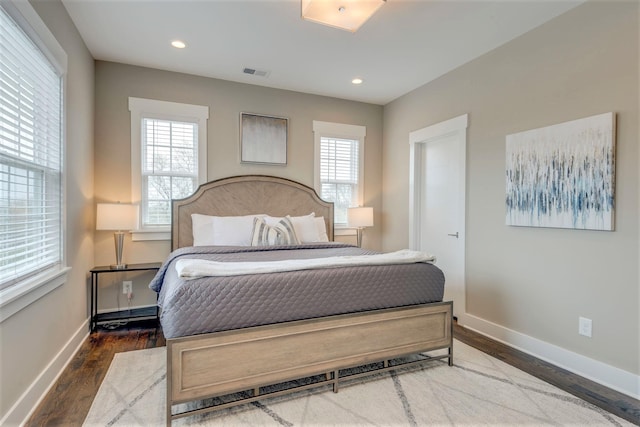 bedroom with multiple windows, wood finished floors, visible vents, and baseboards