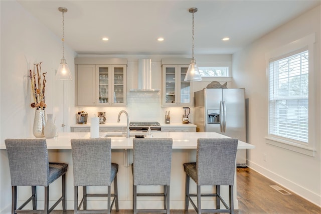 kitchen with visible vents, wall chimney range hood, a breakfast bar area, decorative backsplash, and stainless steel refrigerator with ice dispenser