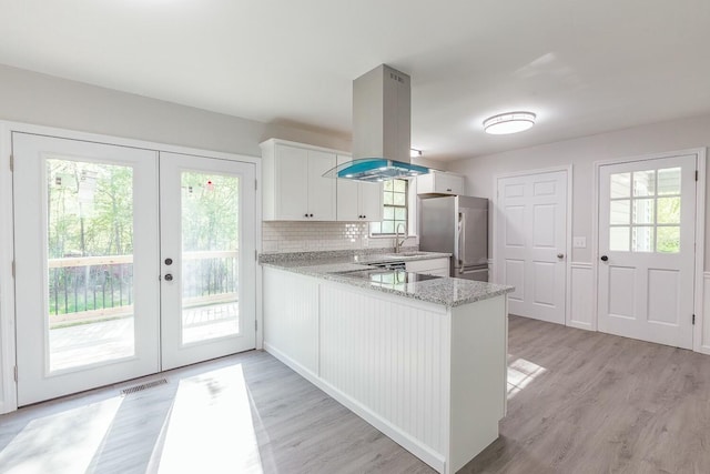 kitchen featuring a sink, white cabinetry, freestanding refrigerator, french doors, and island range hood