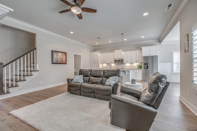 living area featuring crown molding, stairway, a ceiling fan, and light wood-type flooring