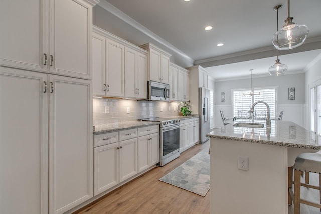 kitchen with a breakfast bar area, ornamental molding, a sink, light wood-style floors, and appliances with stainless steel finishes