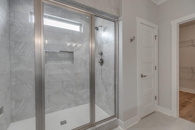 full bathroom with a walk in closet, a shower stall, and baseboards