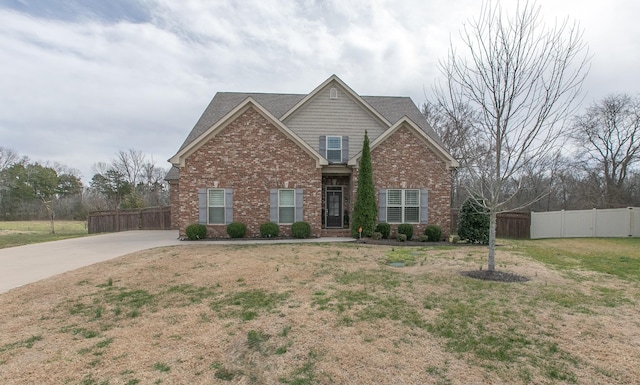 craftsman inspired home featuring driveway, brick siding, a front lawn, and fence