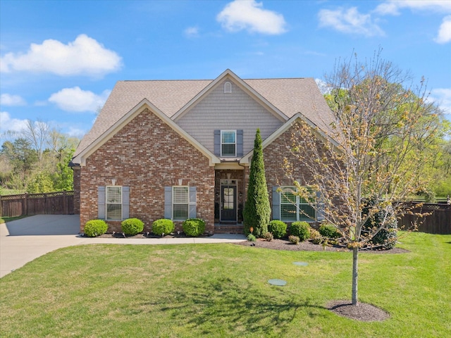 view of front of home featuring brick siding, roof with shingles, a front yard, and fence