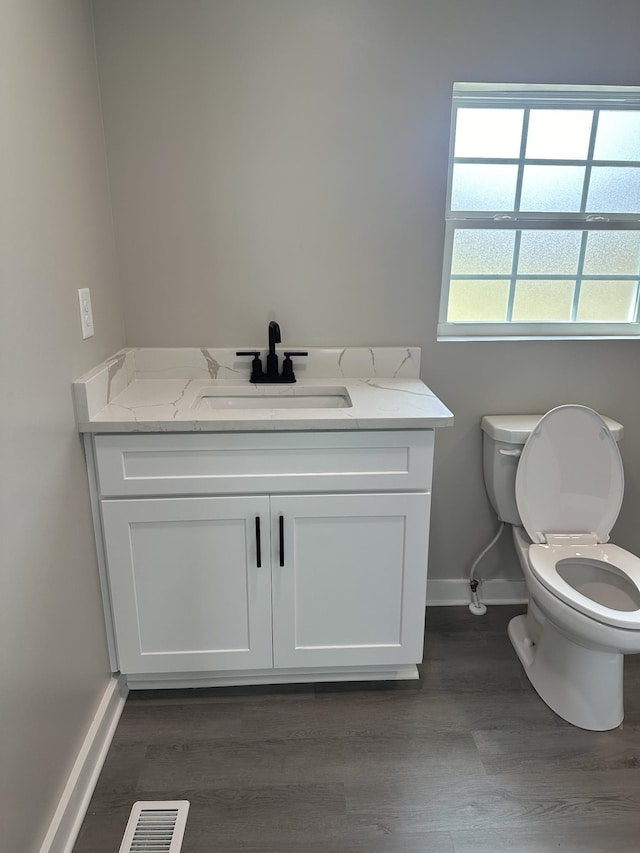 half bath with visible vents, toilet, wood finished floors, baseboards, and vanity