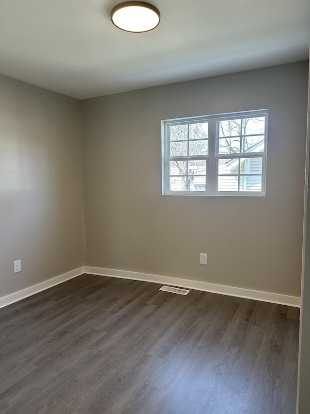 empty room with dark wood-style floors, visible vents, and baseboards