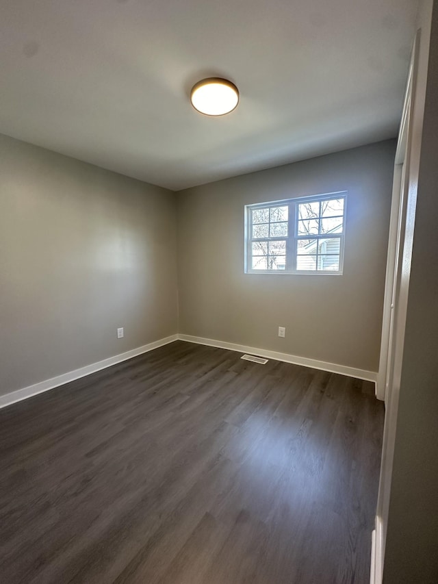 empty room featuring visible vents, baseboards, and dark wood-style floors