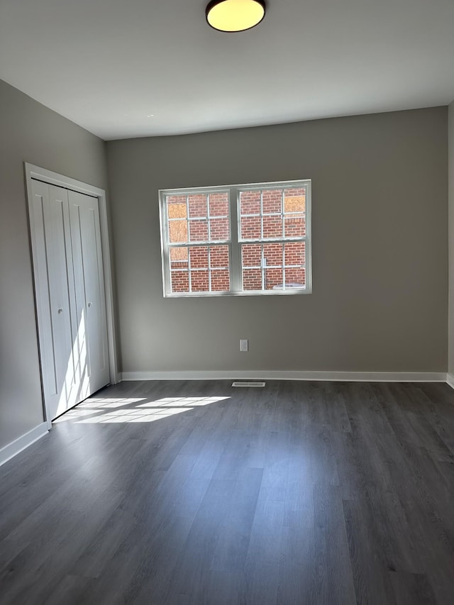 unfurnished bedroom with dark wood-style floors, a closet, and baseboards