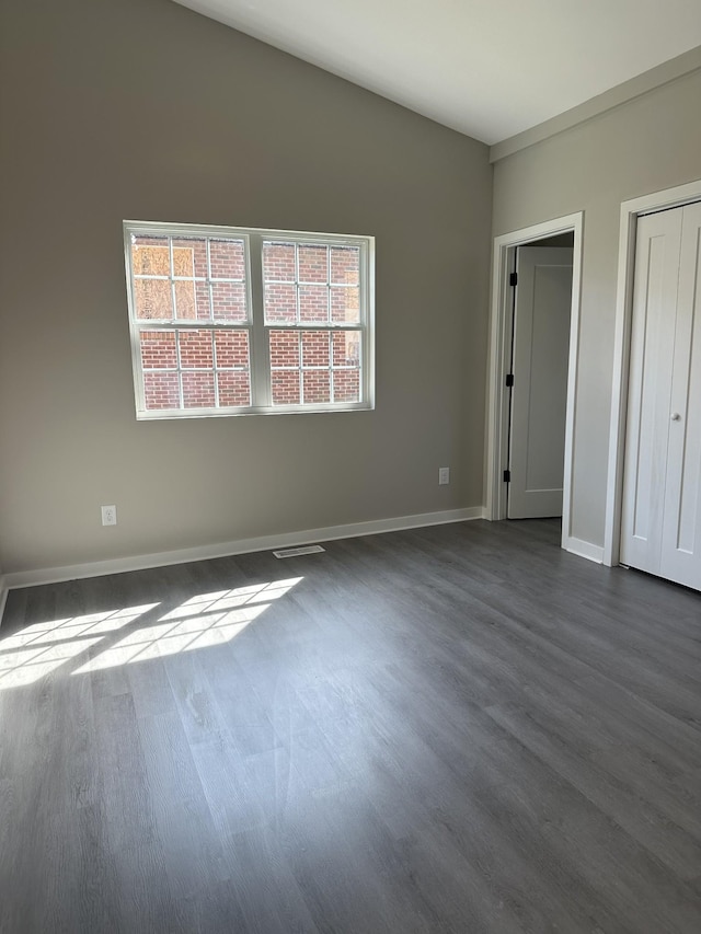 unfurnished bedroom featuring visible vents, lofted ceiling, dark wood-type flooring, and baseboards