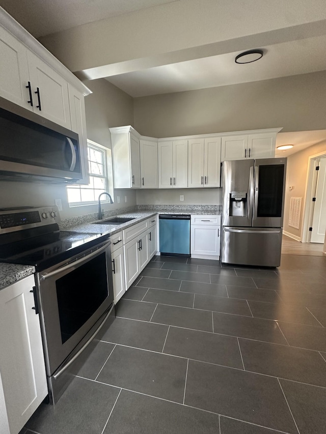 kitchen featuring light stone countertops, a sink, white cabinets, appliances with stainless steel finishes, and dark tile patterned floors