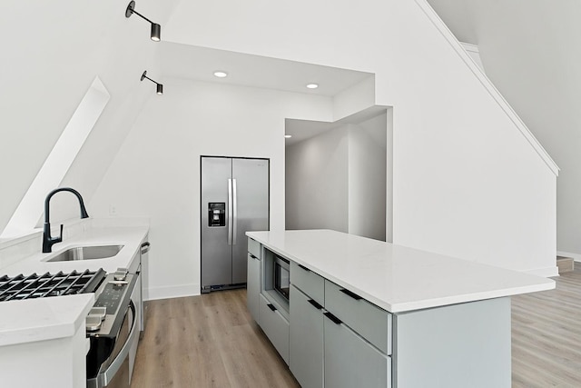 kitchen featuring a sink, a kitchen island, light wood-style floors, and appliances with stainless steel finishes