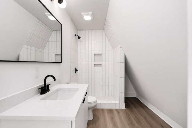 bathroom with vanity, wood finished floors, baseboards, tiled shower, and toilet