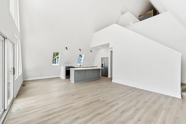 unfurnished living room with a high ceiling, light wood-style floors, baseboards, and a sink