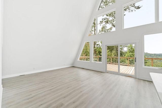 unfurnished living room with baseboards, a healthy amount of sunlight, a towering ceiling, and light wood finished floors