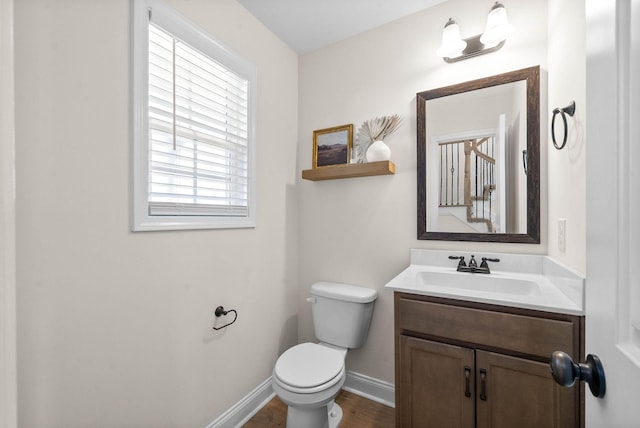 half bathroom with baseboards, toilet, wood finished floors, and vanity