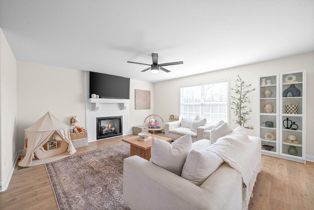 living room with a large fireplace, wood finished floors, and a ceiling fan