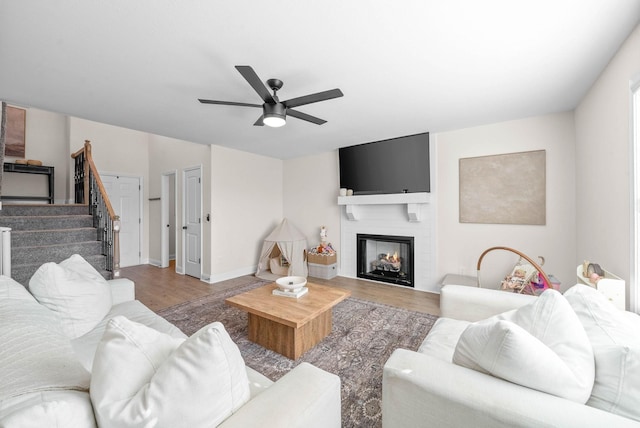 living room featuring stairway, a ceiling fan, wood finished floors, baseboards, and a large fireplace