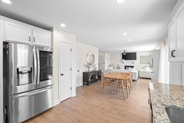 kitchen with light stone countertops, a fireplace, light wood-style floors, stainless steel refrigerator with ice dispenser, and white cabinetry