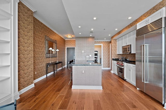 kitchen with premium appliances, white cabinets, wallpapered walls, and crown molding