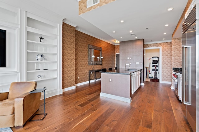 kitchen with wallpapered walls, crown molding, an island with sink, and visible vents