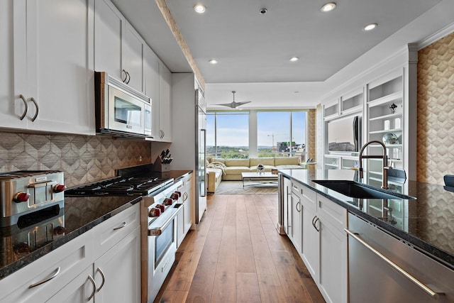 kitchen featuring backsplash, dark stone counters, premium appliances, light wood-style floors, and a sink