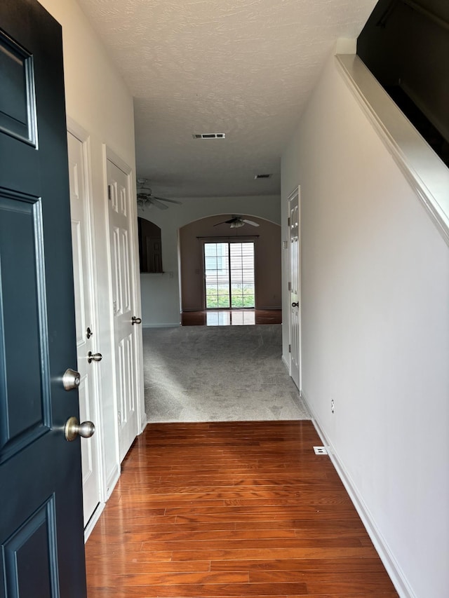 corridor featuring visible vents, carpet flooring, wood finished floors, arched walkways, and a textured ceiling