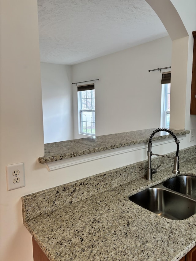 room details with a sink, arched walkways, a textured ceiling, and light stone counters