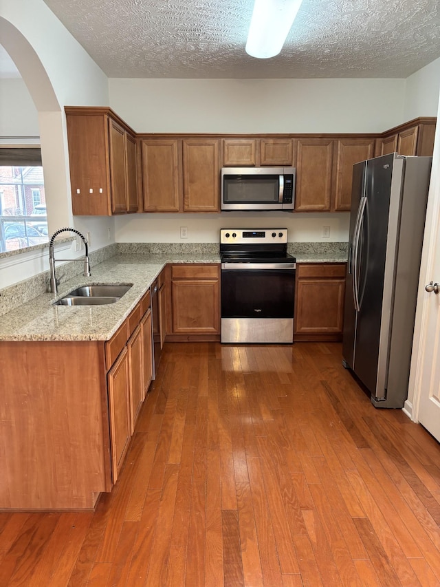 kitchen with light stone countertops, appliances with stainless steel finishes, arched walkways, dark wood-style floors, and a sink