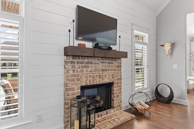 living area featuring a brick fireplace, crown molding, baseboards, and wood finished floors