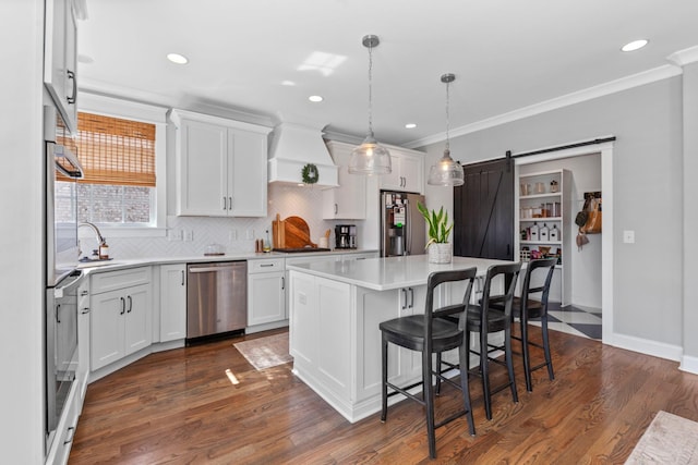 kitchen with custom exhaust hood, ornamental molding, stainless steel appliances, white cabinets, and a barn door