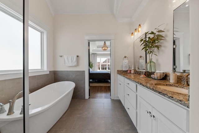 ensuite bathroom featuring double vanity, a soaking tub, ornamental molding, tile patterned flooring, and a sink