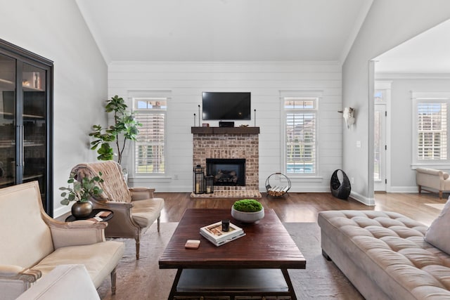 living area featuring baseboards, wood finished floors, a fireplace, and ornamental molding