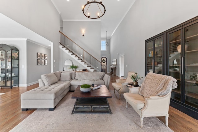 living area featuring wood finished floors, baseboards, ornamental molding, stairs, and a notable chandelier