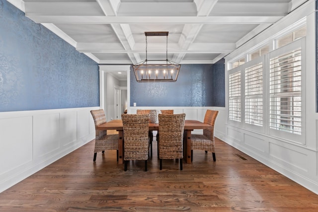 dining space with wood finished floors, a wainscoted wall, an inviting chandelier, beam ceiling, and a decorative wall