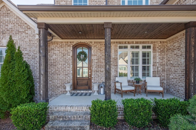 view of exterior entry with brick siding and a porch