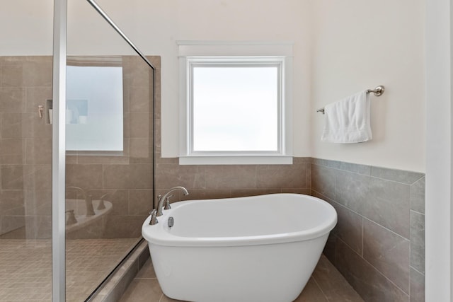 bathroom featuring a shower stall, a freestanding tub, tile walls, and a wainscoted wall