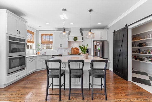 kitchen featuring premium range hood, light countertops, appliances with stainless steel finishes, white cabinetry, and a barn door