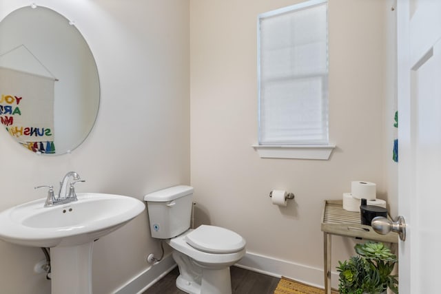 half bathroom featuring toilet, wood finished floors, baseboards, and a sink