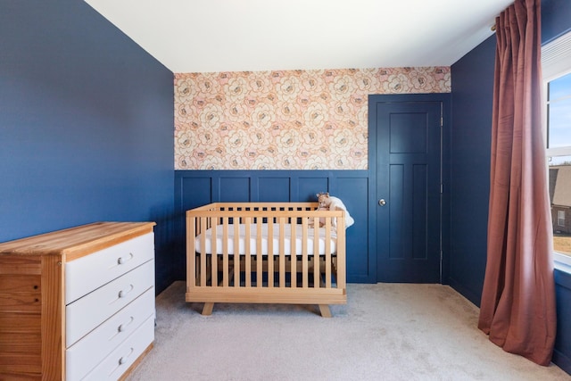 bedroom featuring carpet flooring, wainscoting, wallpapered walls, and a crib