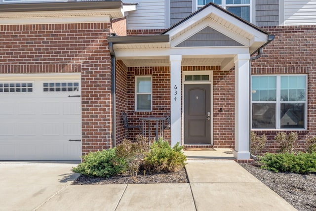 view of exterior entry with a garage, brick siding, and driveway