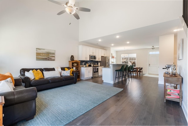 living room featuring baseboards, ceiling fan, recessed lighting, a high ceiling, and dark wood-style floors