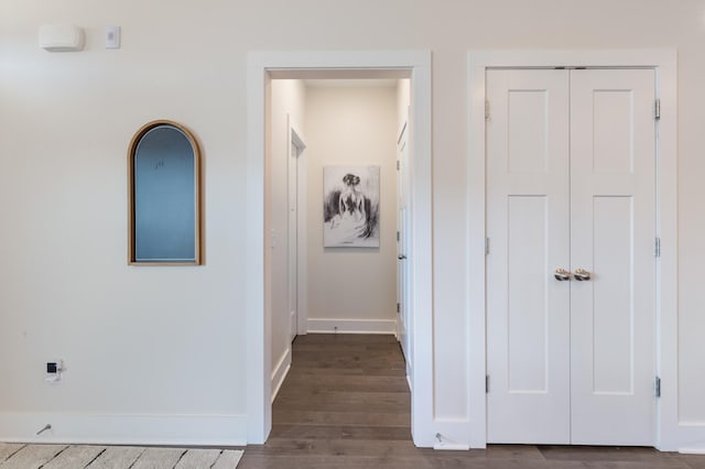 corridor featuring dark wood-type flooring and baseboards