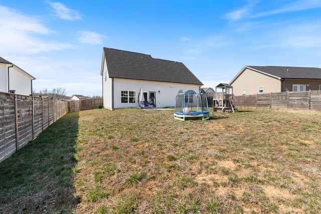 rear view of property with a fenced backyard, a lawn, and a trampoline