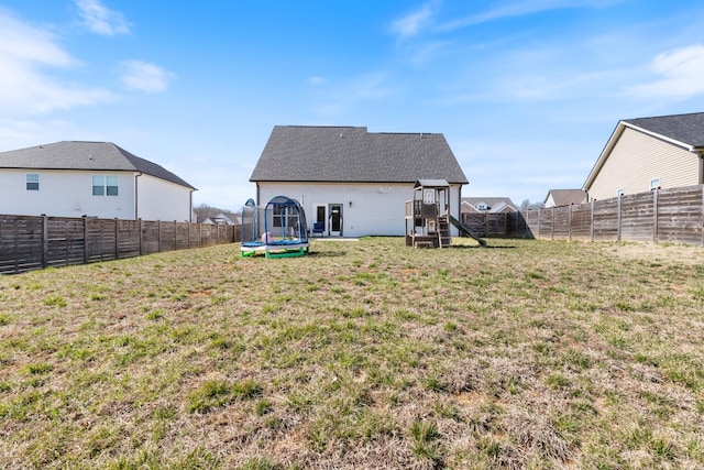 rear view of house with a yard, a fenced backyard, and a trampoline