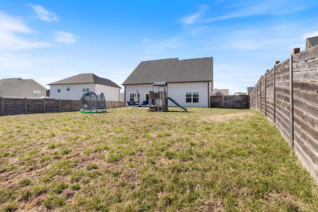 back of house featuring a trampoline, a fenced backyard, and a yard