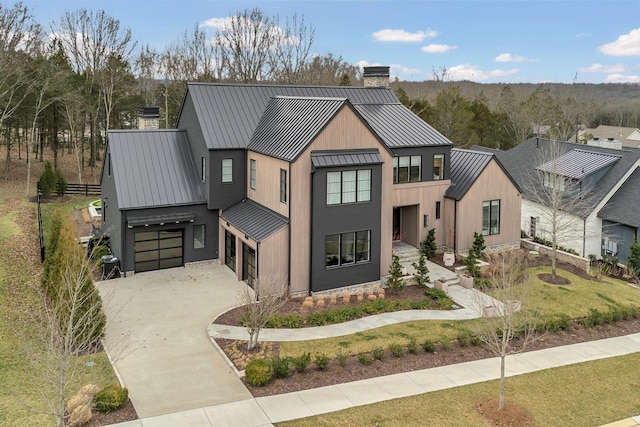 modern farmhouse featuring concrete driveway, a chimney, metal roof, a garage, and a standing seam roof