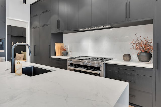 kitchen with modern cabinets, a sink, double oven range, tasteful backsplash, and light stone countertops