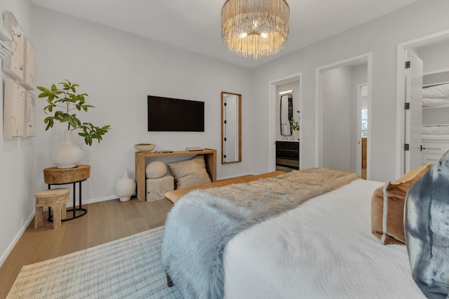 bedroom featuring a chandelier, connected bathroom, baseboards, and wood finished floors