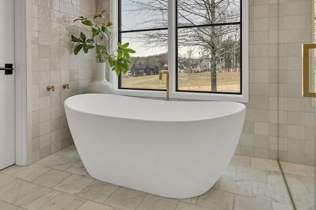 full bathroom featuring marble finish floor, tile walls, and a freestanding tub